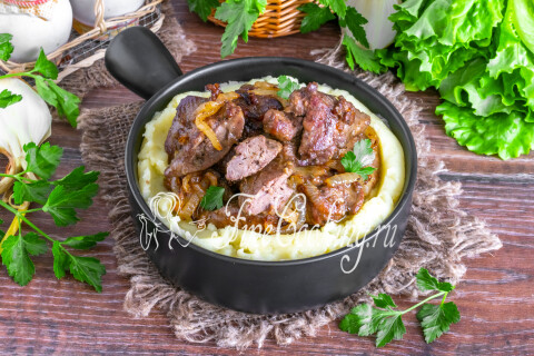 Порция жареной куриной печени с луком и картофельным пюре на тарелке